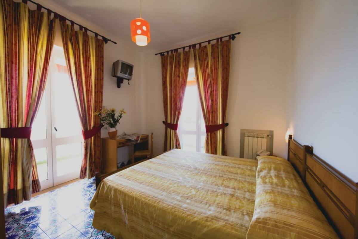 A hotel room with a large bed, curtains, a desk with a chair, and a TV on the wall.