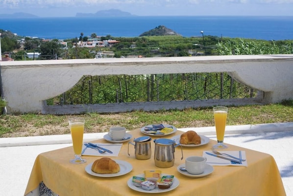 Mesa lista para el desayuno con vista al océano y una colina al fondo.