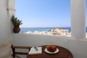 A balcony with a view of the sea and buildings, a wooden table with a book and fruit. - Panorama (Naxos)