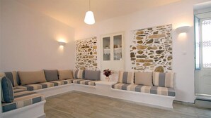 A living room with a sectional sofa, stone wall decor, and a pendant light. - Panorama (Naxos)