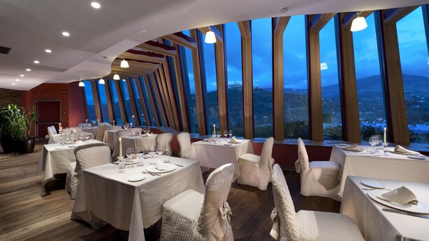 A restaurant with round tables, white chairs, and large windows offering a view of the landscape. - Hotel Bouganville (Picerno)