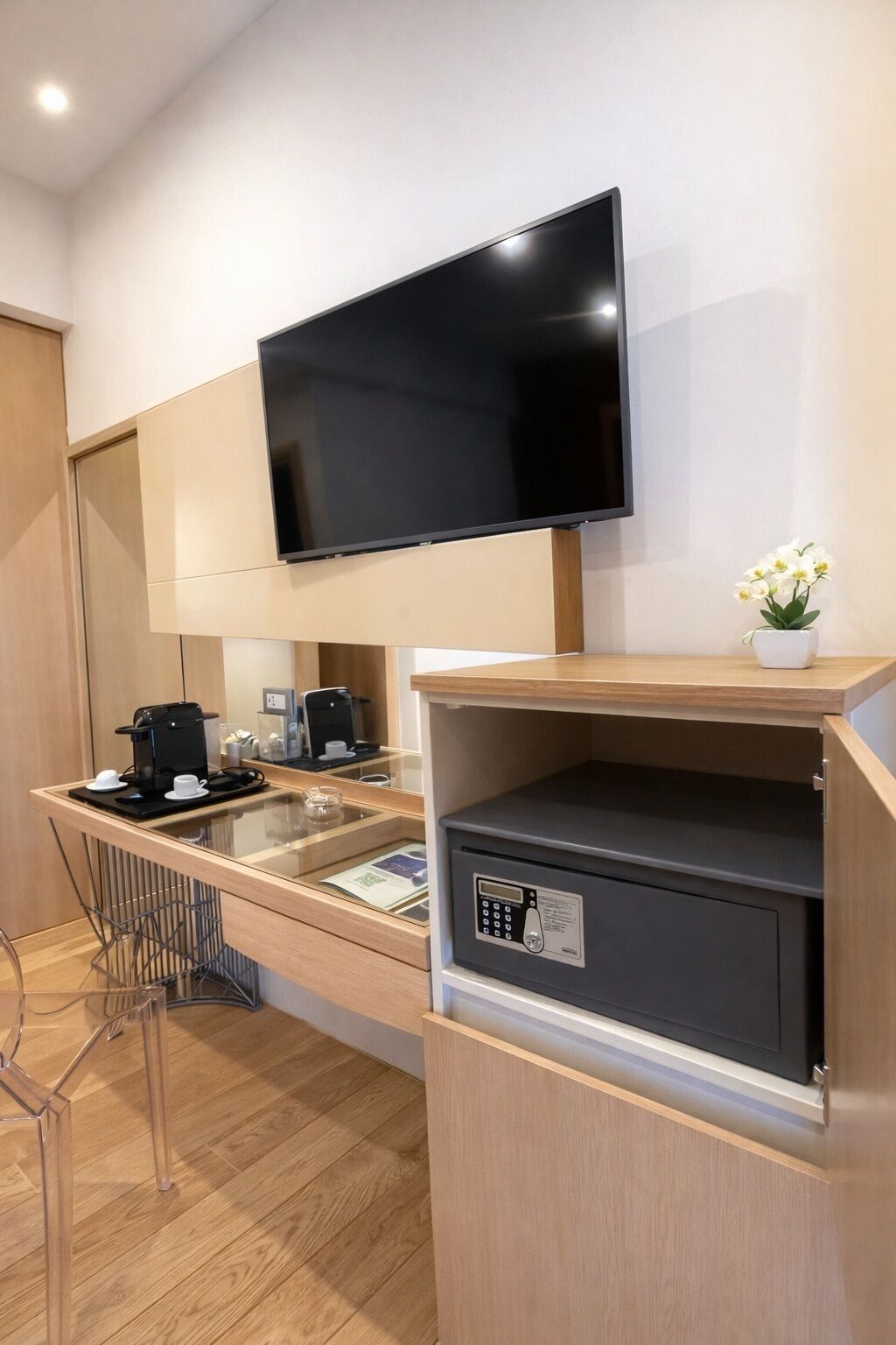 Habitació d'hotel moderna amb televisió de pantalla plana penjada a la paret, una cafetera i una caixa forta.