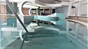 An indoor swimming pool with a modern design, featuring a central staircase and a glass barrier. - Hotel Bouganville (Picerno)