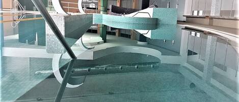 Piscina interna com design moderno, com uma escadaria central e barreira de vidro.