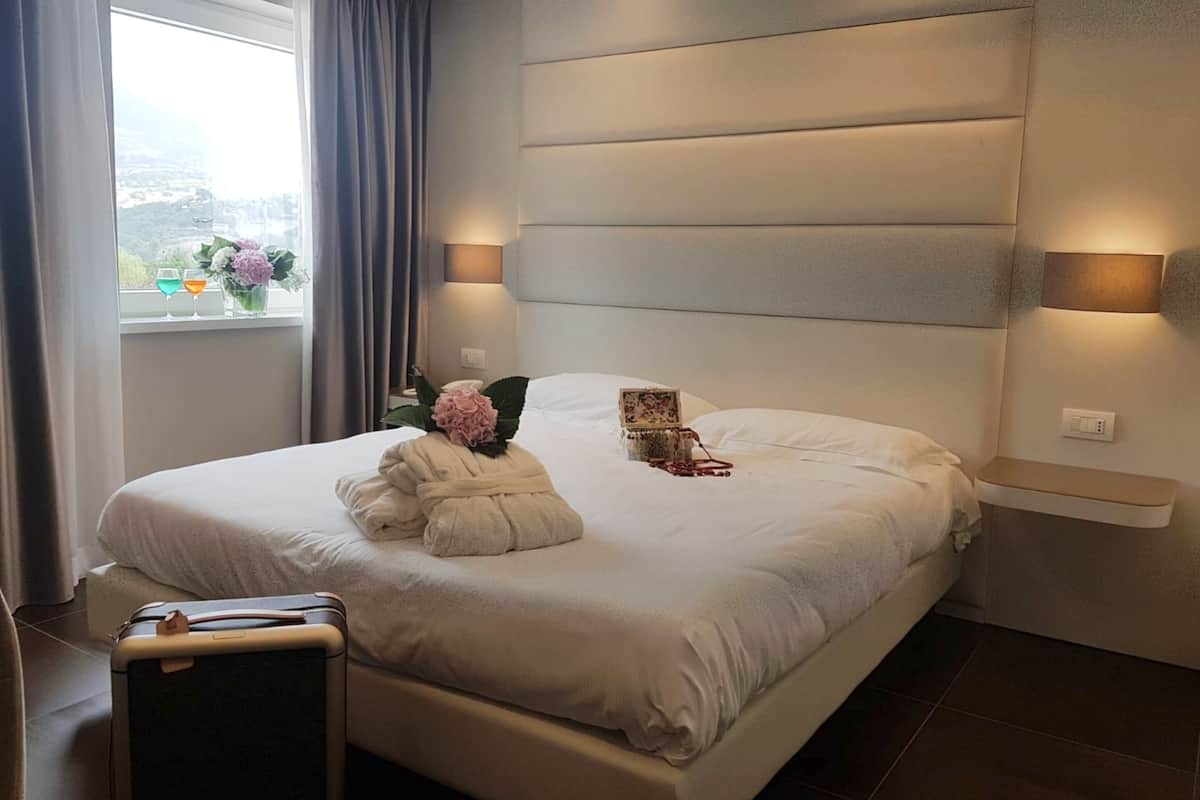 Een moderne hotelkamer met een groot bed, een nachtkastje, een raam met gordijnen en uitzicht op de stad.