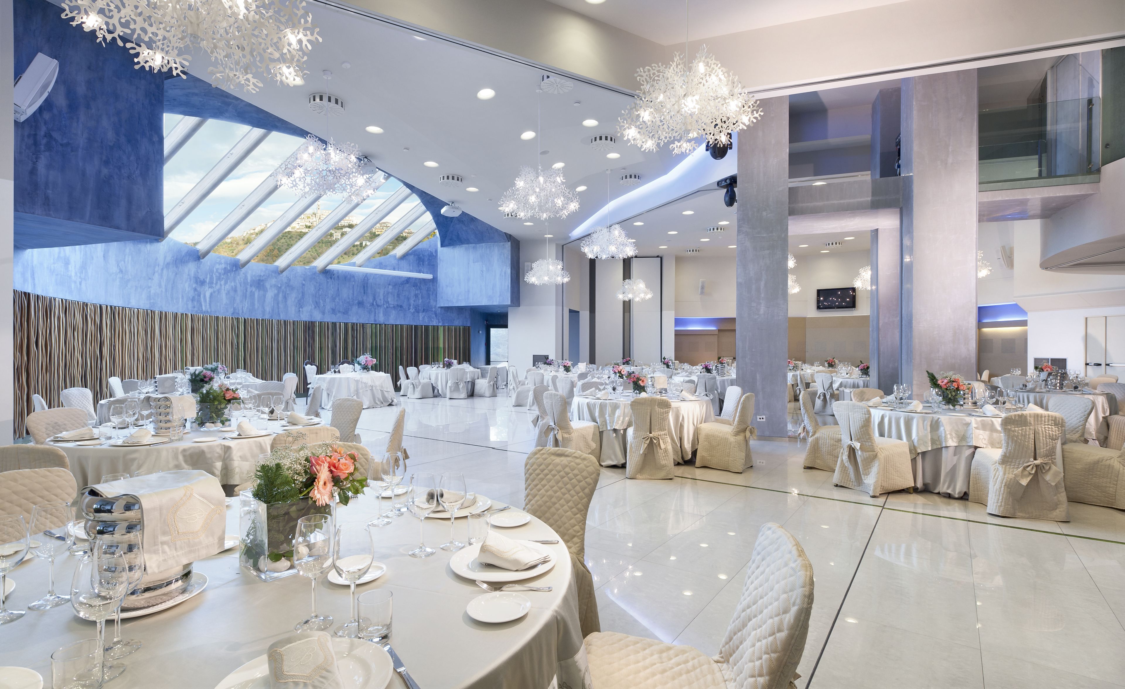 Un amplio salón de banquetes con varias mesas redondas dispuestas para cenar, con manteles blancos y elegantes centros de mesa.