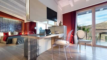 Ein modernes Wohnzimmer mit Holzboden, einer Sofagarnitur, einem Essbereich mit Tisch und einem großen Fenster mit Blick ins Freie.