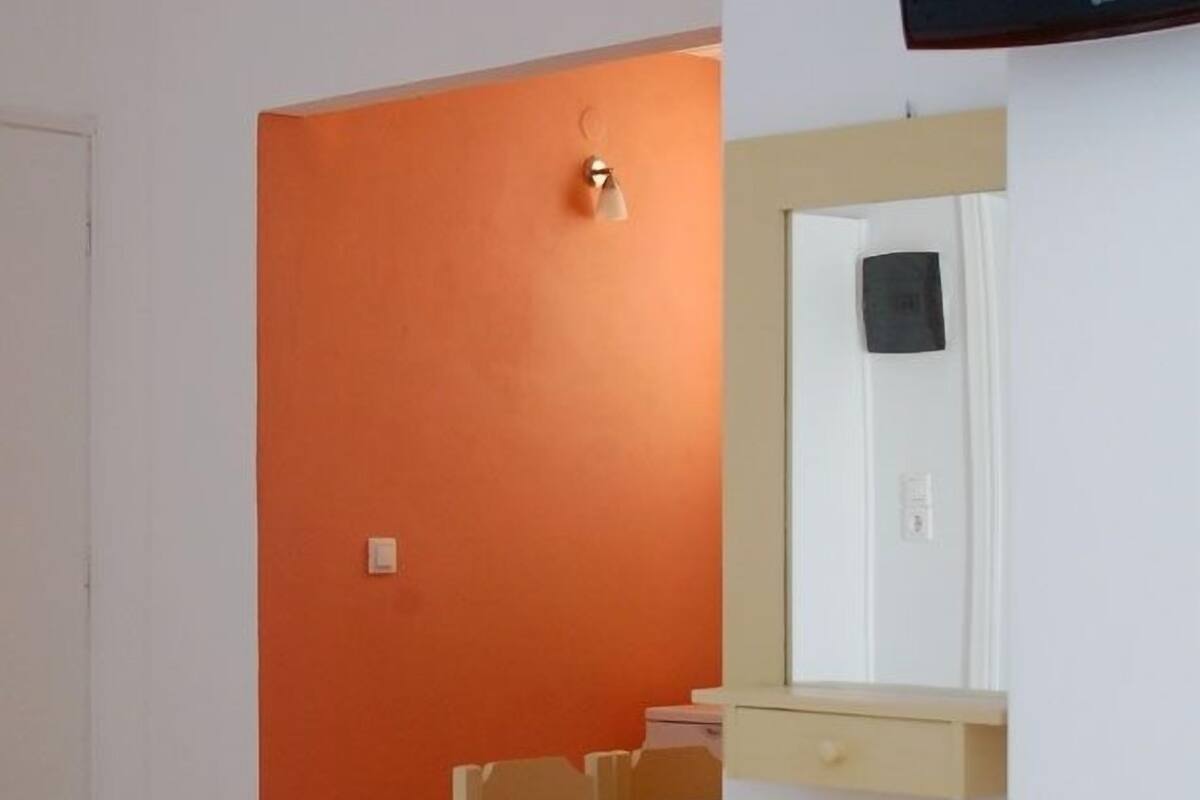A room with a bed, a desk, a chair, a television, and a trash bin.