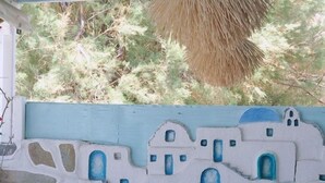 Un patio con mobiliario de madera y una pared pintada para simular un pueblo griego.