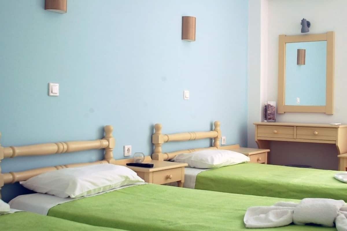 A hotel room with two wooden beds, green bedspreads, a wooden nightstand, a small table, a mirror, and a light fixture.
