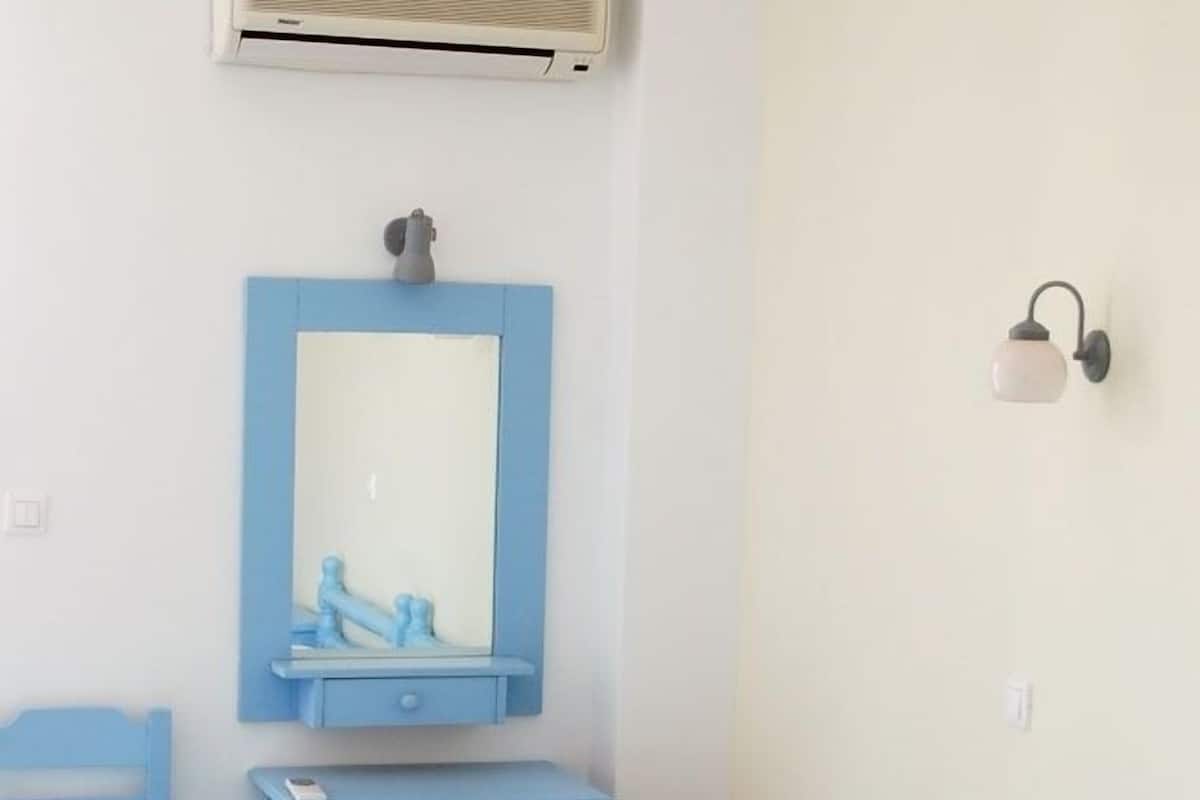 A room with two beds, a small desk, a chair, a mirror, a wall-mounted light, and an air conditioning unit.