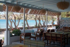 A covered outdoor seating area with wooden furniture and a view of the sea. - Hotel Paros (Paros)