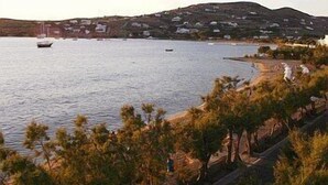 Vista costera con barcos en el agua, una playa con árboles y una colina con edificios.