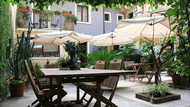 An outdoor patio with a wooden table and chairs, surrounded by potted plants and umbrellas. - Casa Barbero Charme & Rooms (Catania)