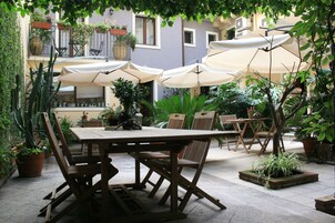 Un patio al aire libre con una mesa y sillas de madera, rodeado de plantas en macetas y sombrillas.