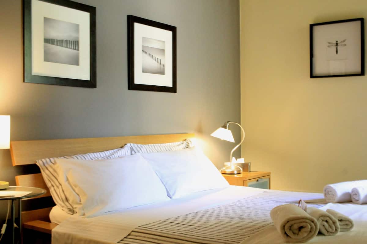 A hotel room with a neatly made bed, a bedside lamp, and framed pictures on the wall.