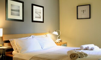 Habitación de hotel con una cama bien hecha, una lámpara de noche y cuadros en la pared.
