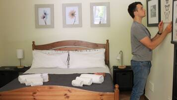 A hotel room with a wooden bed, white pillows, and towels on the bed. There are framed pictures on the wall above the bed.