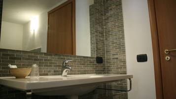A bathroom with a white sink, a wooden bowl, a glass, and a mirror.