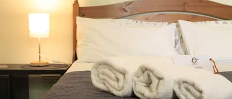 A neatly made bed with a dark patterned bedspread, a wooden headboard, and a bedside table with a lamp.