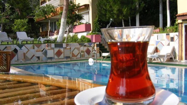 A glass of tea on a table by a pool with lounge chairs and a tiled wall. - Asia Apart Hotel (Kusadasi)