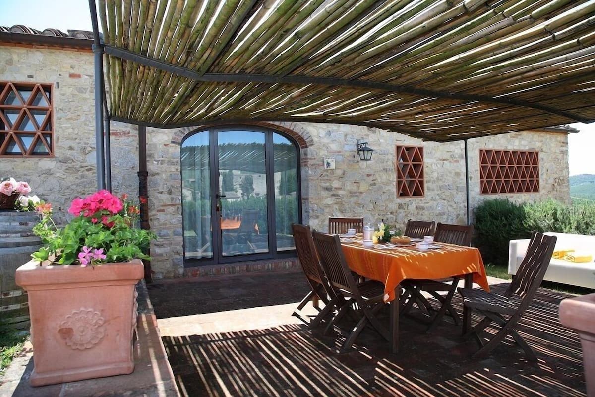 Un patio al aire libre con mesa y sillas, una planta en maceta y un edificio de piedra con ventanas.