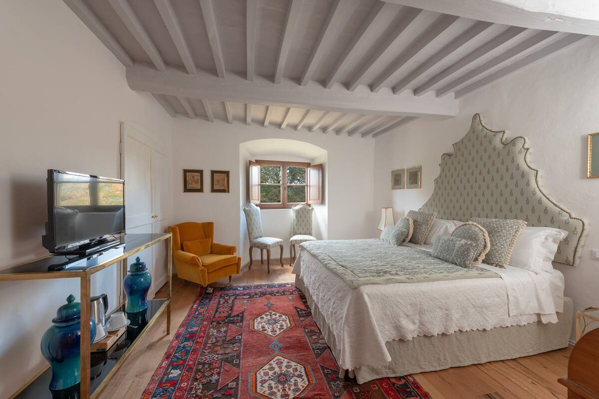 Un dormitorio con cama, televisión, silla y ventana.