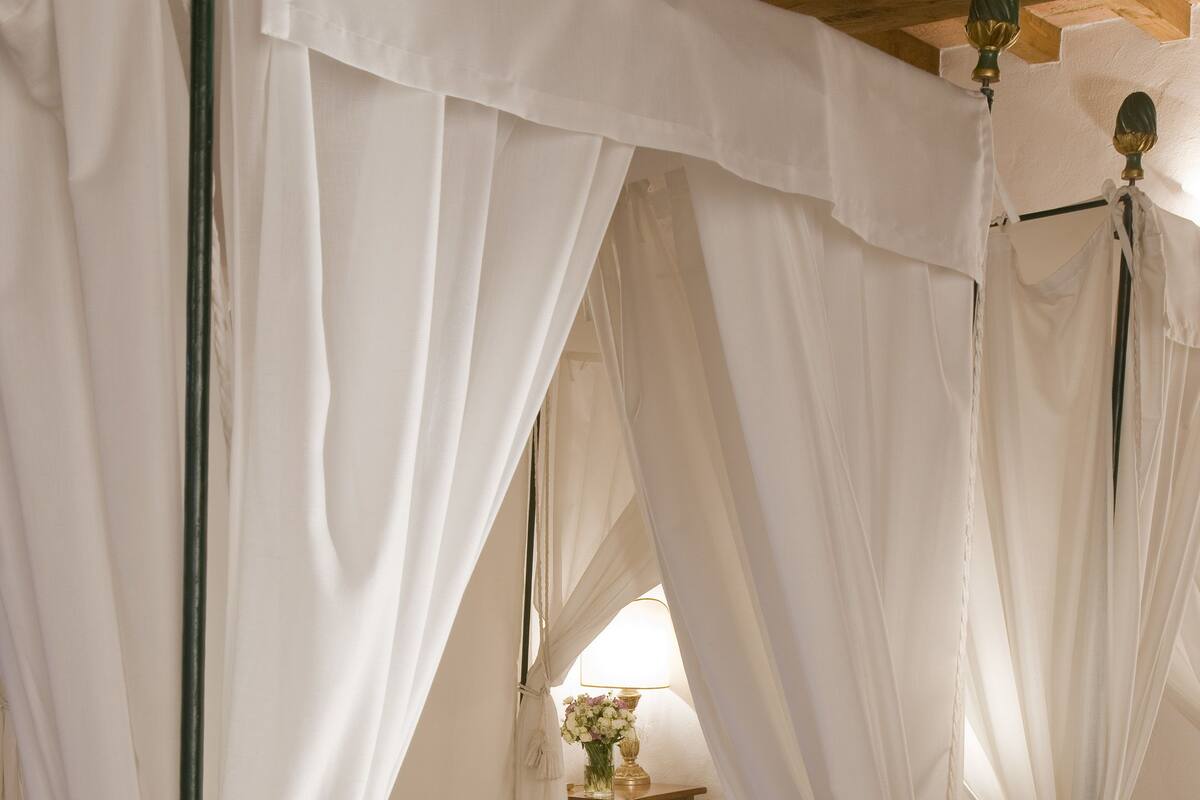 Un dormitorio con cama a dosel, una mesita de noche con lámpara y un arreglo floral.