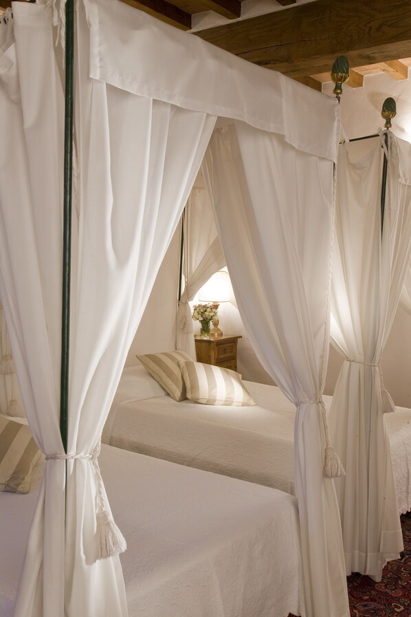 A bedroom with a canopy bed, a bedside table with a lamp, and a floral arrangement.