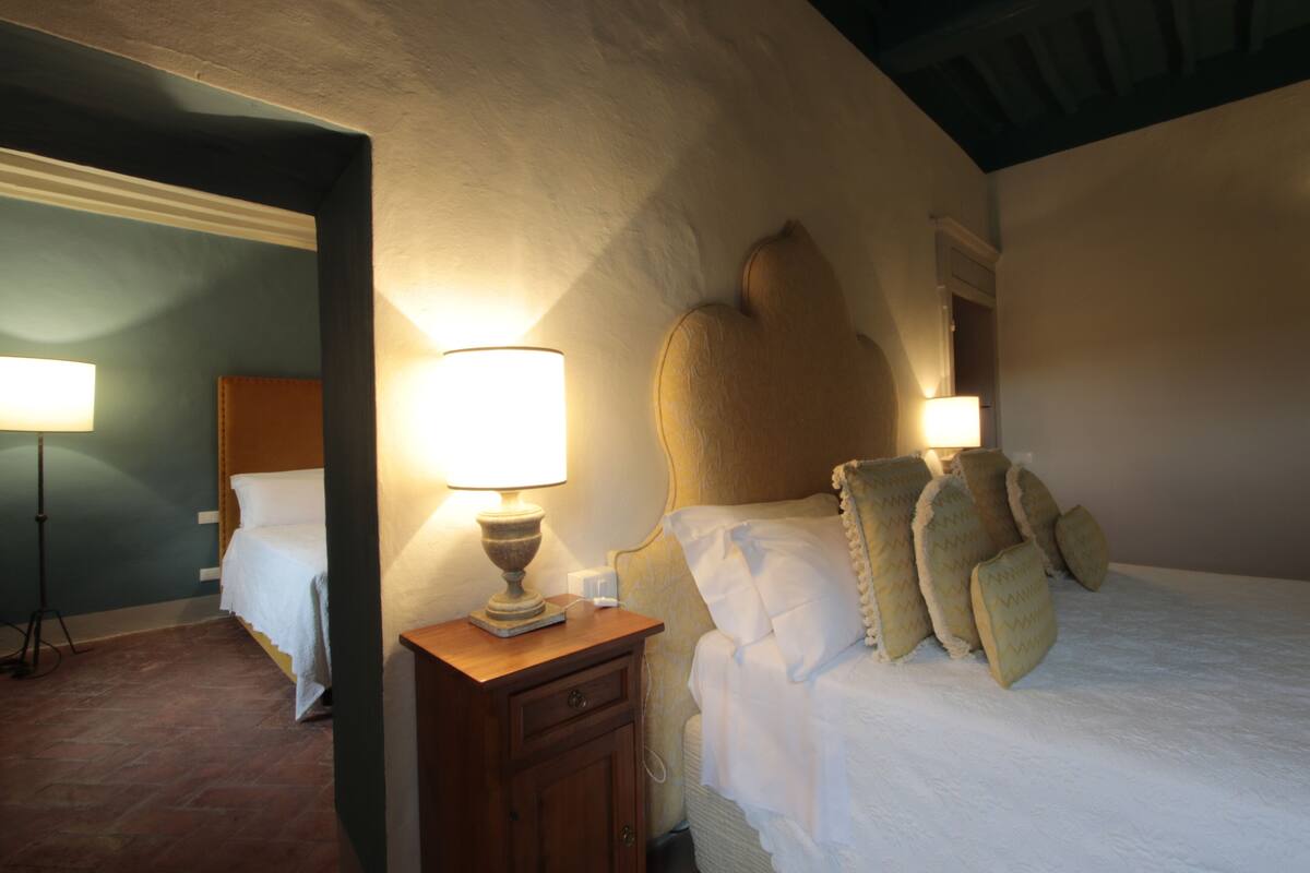 Un dormitorio con una cama grande, una mesita de noche con lámpara y otra mesita.