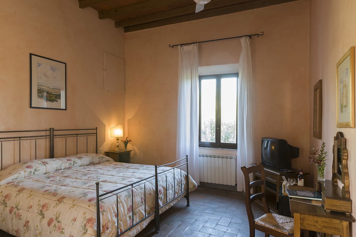 Un dormitorio con cama, escritorio, silla, televisión y ventana con cortinas.