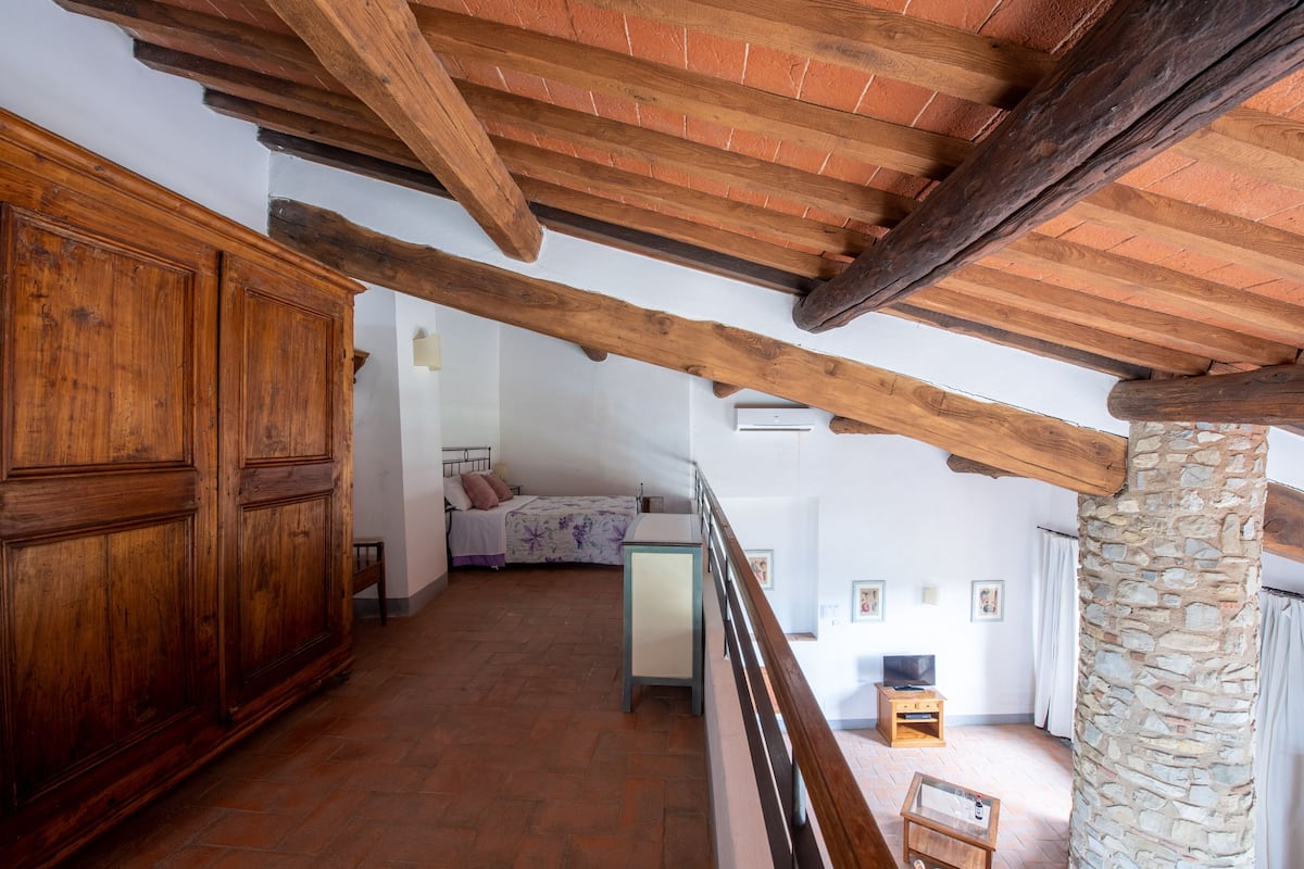 Una habitación rústica con vigas de madera a la vista, un pilar de piedra, una cama con colcha estampada y una pequeña mesa de madera.