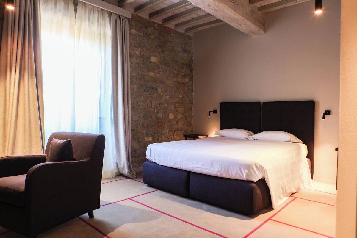 Un dormitorio con cama, una silla, pared de piedra y techo de madera.