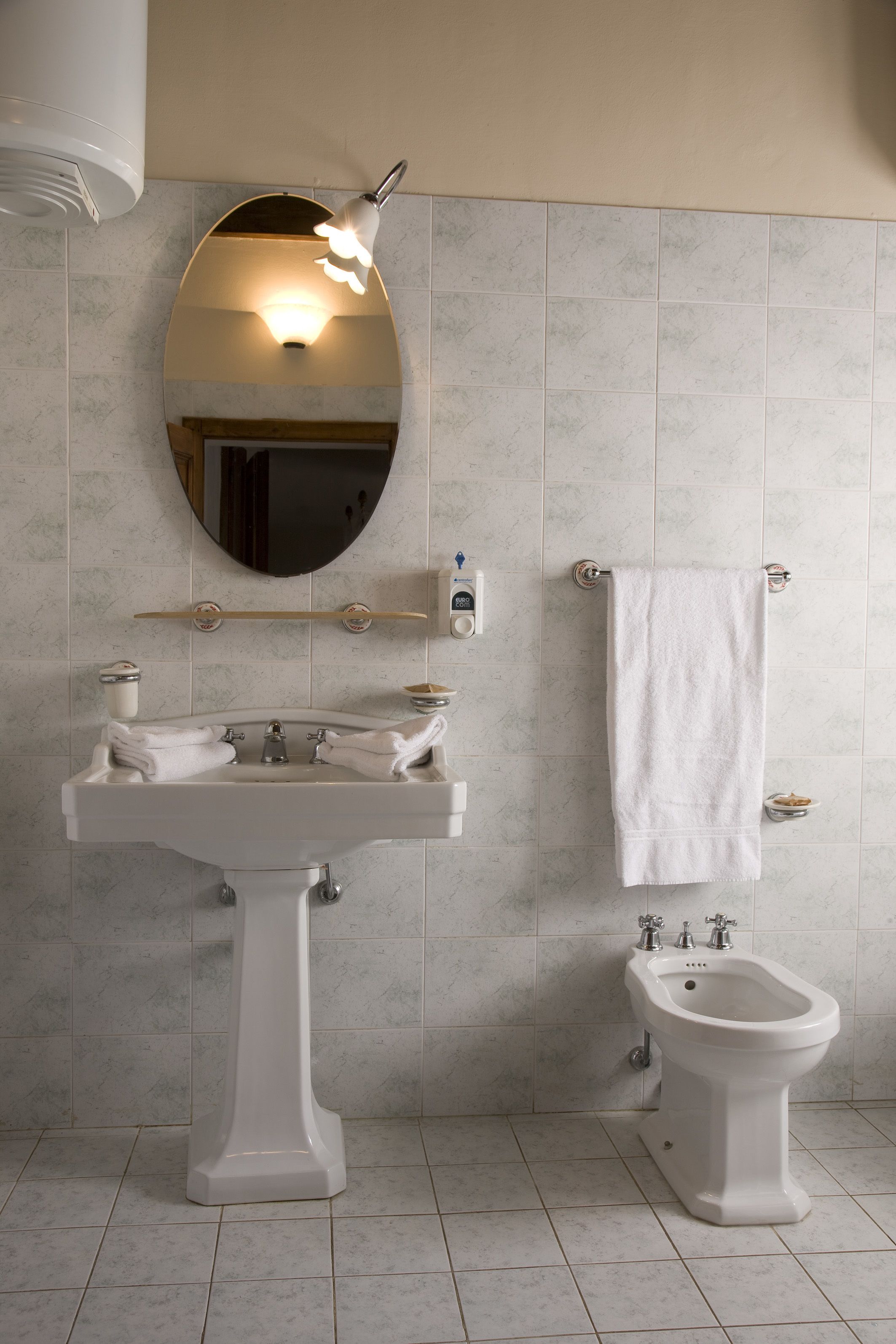 Un baño con lavamanos pedestal, un bidé, un perchero y un espejo.