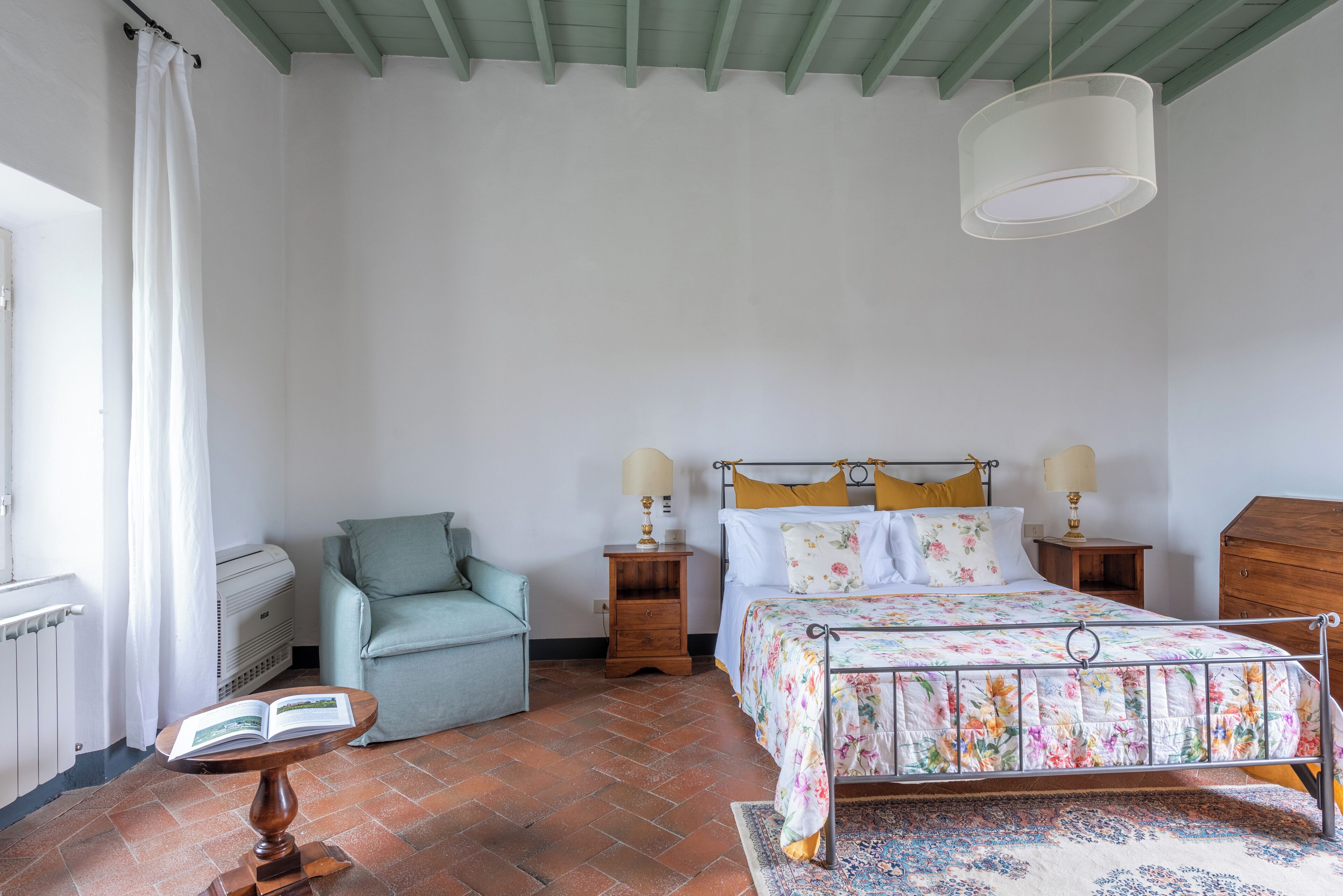 A bedroom with a bed, a chair, a table with a book, and a radiator.