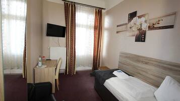 Ein Hotelzimmer mit einem Bett, einem Schreibtisch, einem Sessel, einem Fernseher und Vorhängen.