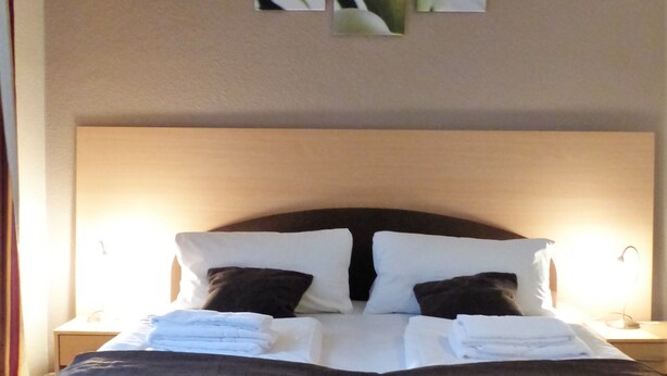 A neatly made bed with white and dark pillows, a quilted blanket, and a headboard. - City Hotel Gotland (Berlin)