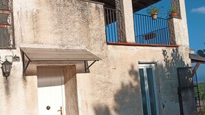 A building with a concrete facade, a metal balcony with a black railing, and a small window with blue shutters.