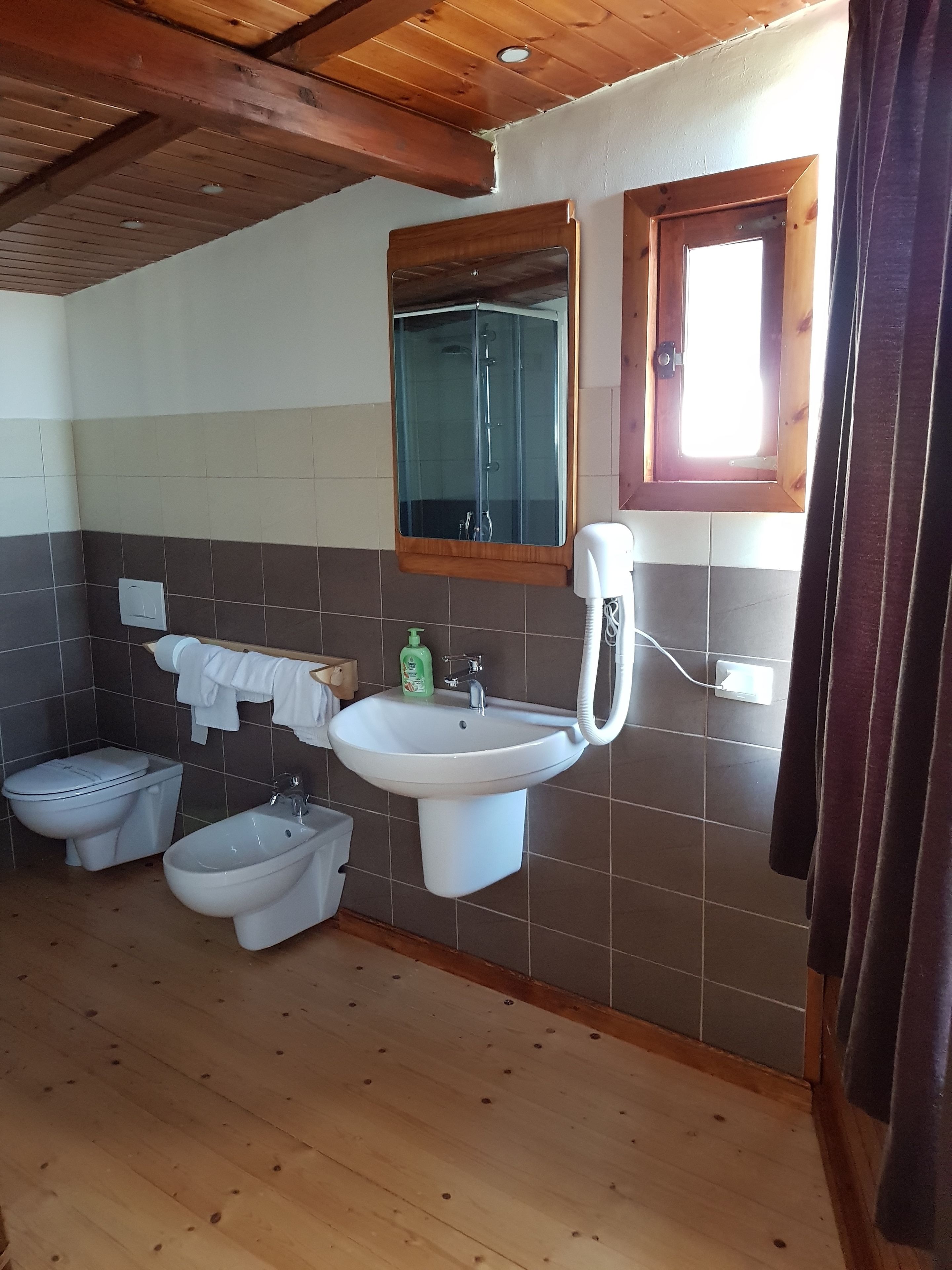 Un baño con techo de madera, un lavamanos, un bidé, un inodoro y un espejo.