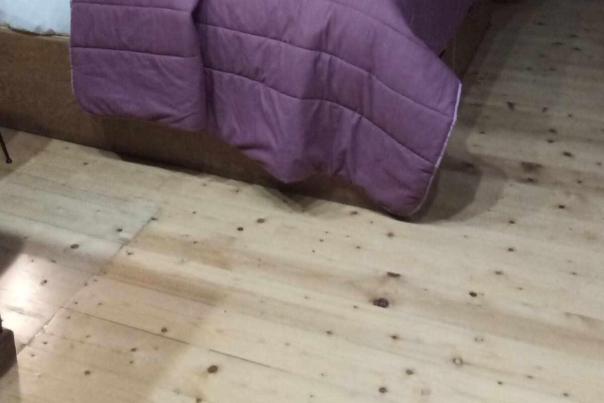 Une pièce de cabane en bois avec un lit, une couverture violette et un panneau accroché au mur.