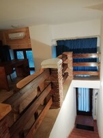 Quarto compacto com beliche, escrivaninha de madeira e janela com cortinas.