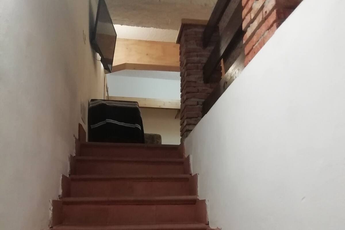 Un escalier aux marches rouges menant vers le haut, flanqué de murs blancs et d’un mur de briques sur la droite.