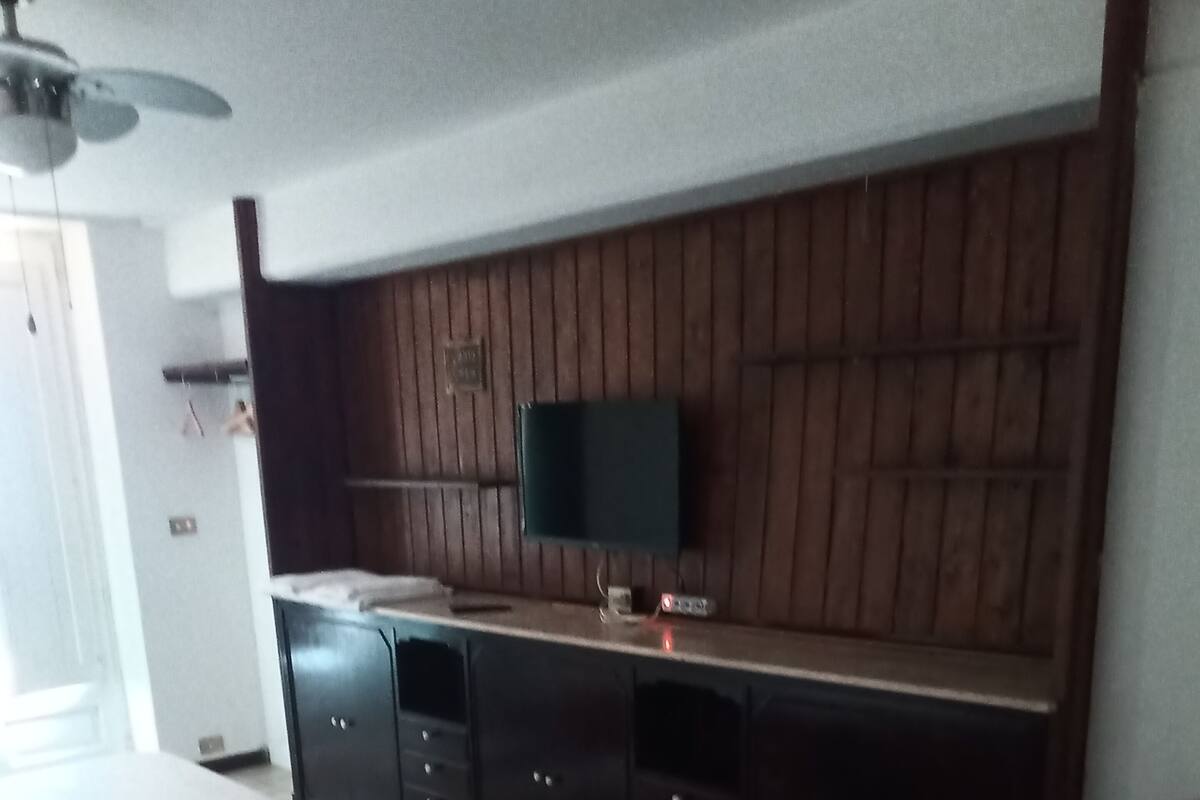Une chambre à coucher avec un lit, un téléviseur fixé au mur (qui est en bois) et une commode.