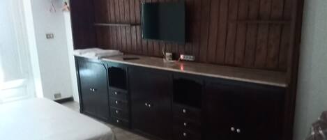 Un dormitorio con una cama, un televisor instalado en una pared de madera y un aparador.