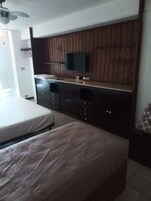 Quarto com uma cama, uma televisão fixada em uma parede de madeira e um aparador.