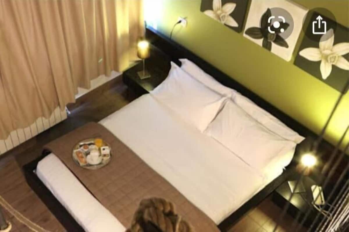 A neatly made bed with pillows and a tray of breakfast items, a bedside table with a lamp, and a wall with floral artwork.