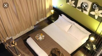 A neatly made bed with pillows and a tray of breakfast items, a bedside table with a lamp, and a wall with floral artwork.