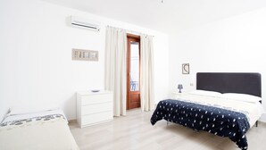 Ein Schlafzimmer mit Bett, Nachttisch, Kommode, einer Tür mit Vorhängen und einer Klimaanlage.