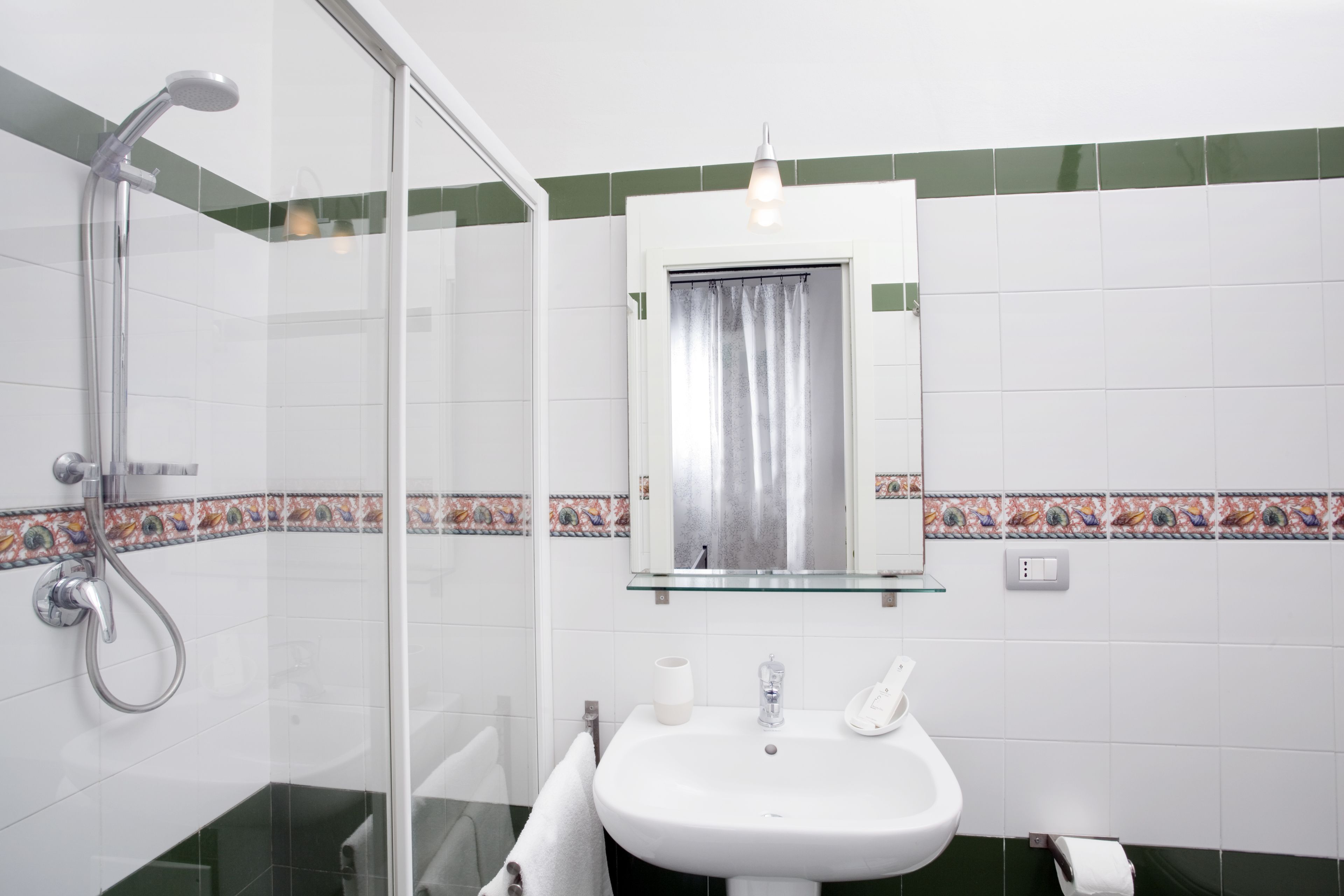 Un bagno con box doccia in vetro, lavandino bianco e specchio sopra.