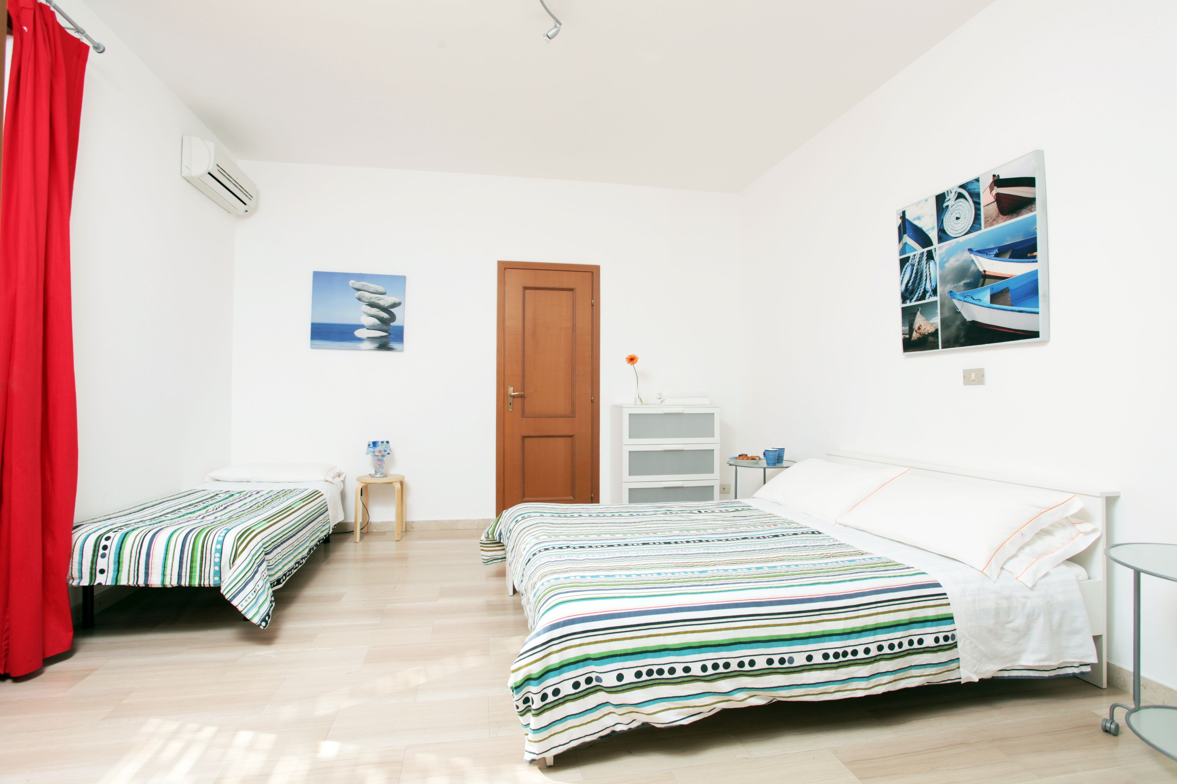 Un dormitorio con dos camas individuales, una puerta de madera, una mesita de noche pequeña y una estantería en la pared.